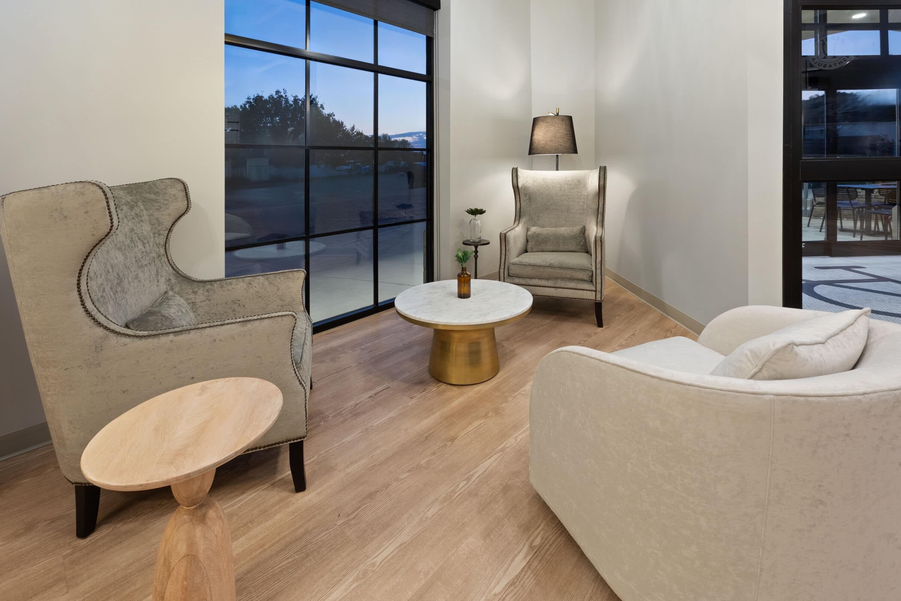 A modern living room with a large window, a round coffee table, and two armchairs.