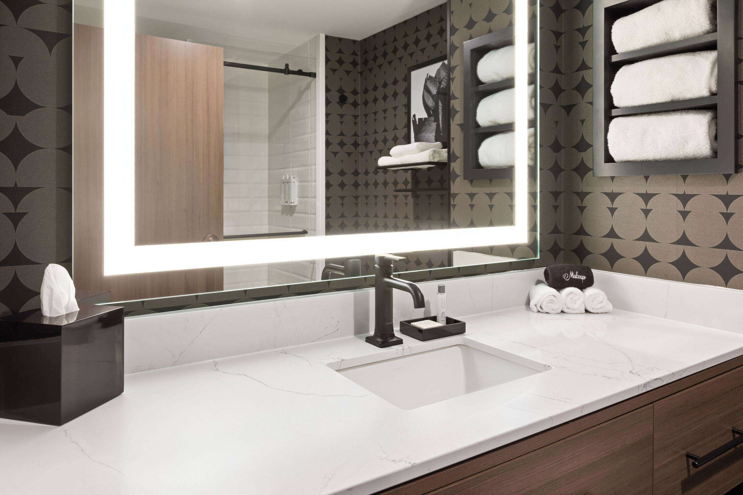 A modern bathroom with a large mirror, a white sink, and a towel rack.