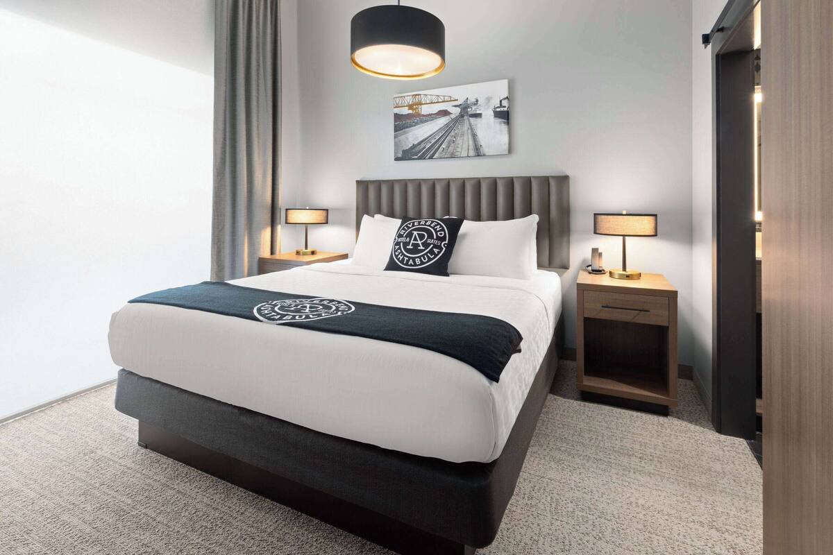 A modern hotel room with a large bed, two bedside tables, a headboard, and a wall-mounted picture.