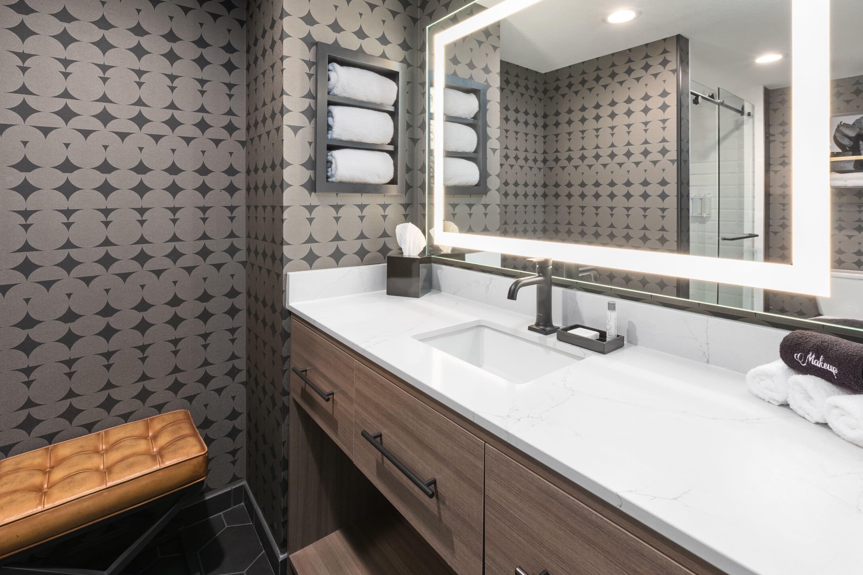 A bathroom with a vanity, mirror, towel rack, and bench.