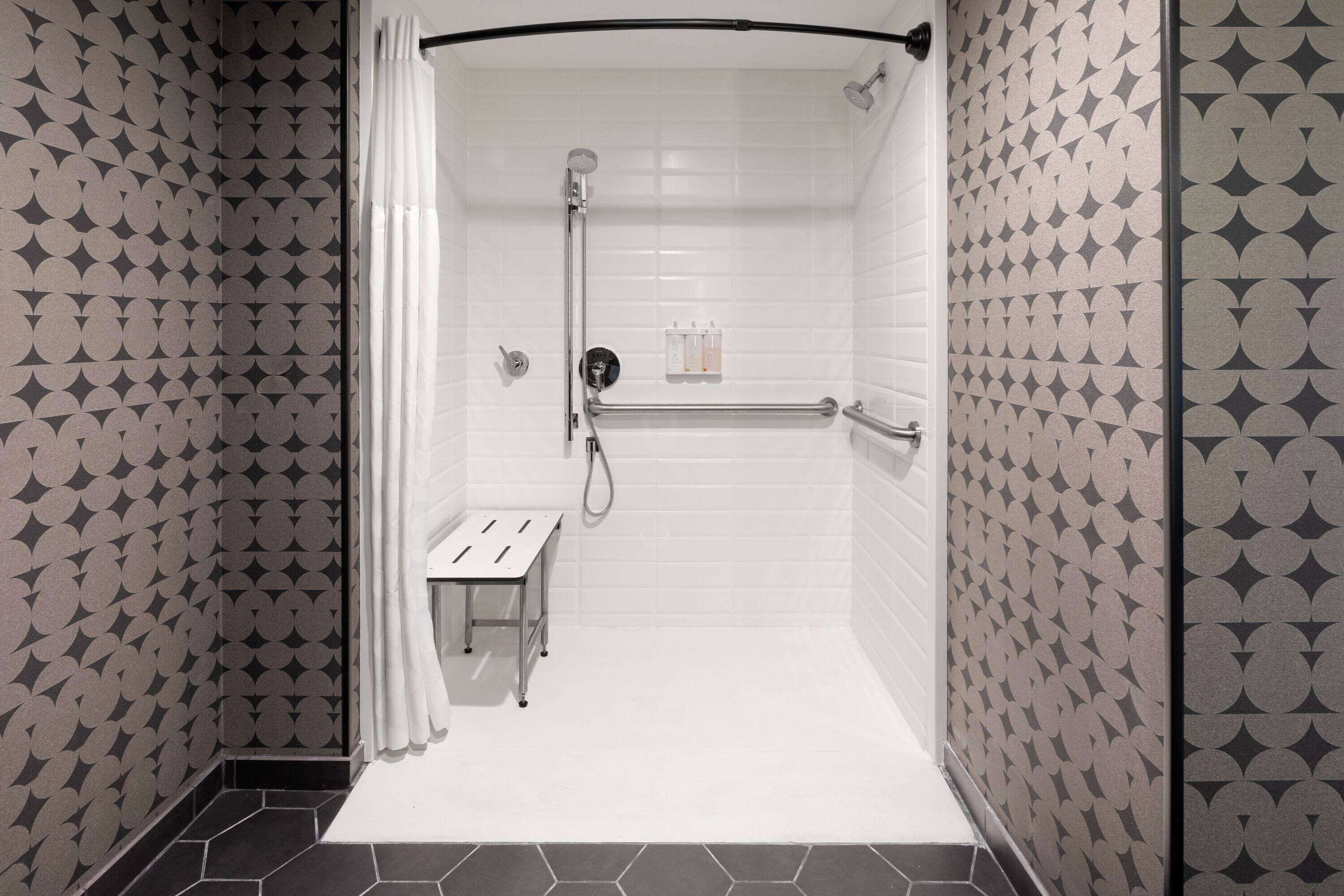 A shower area with a white tiled wall, a showerhead, a handheld shower, and a bench.