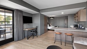 A modern kitchen with a dining area, bar stools, and a flat-screen TV. - Riverbend Hotel and Suites, Trademark Collection by Wyndham (Ashtabula)