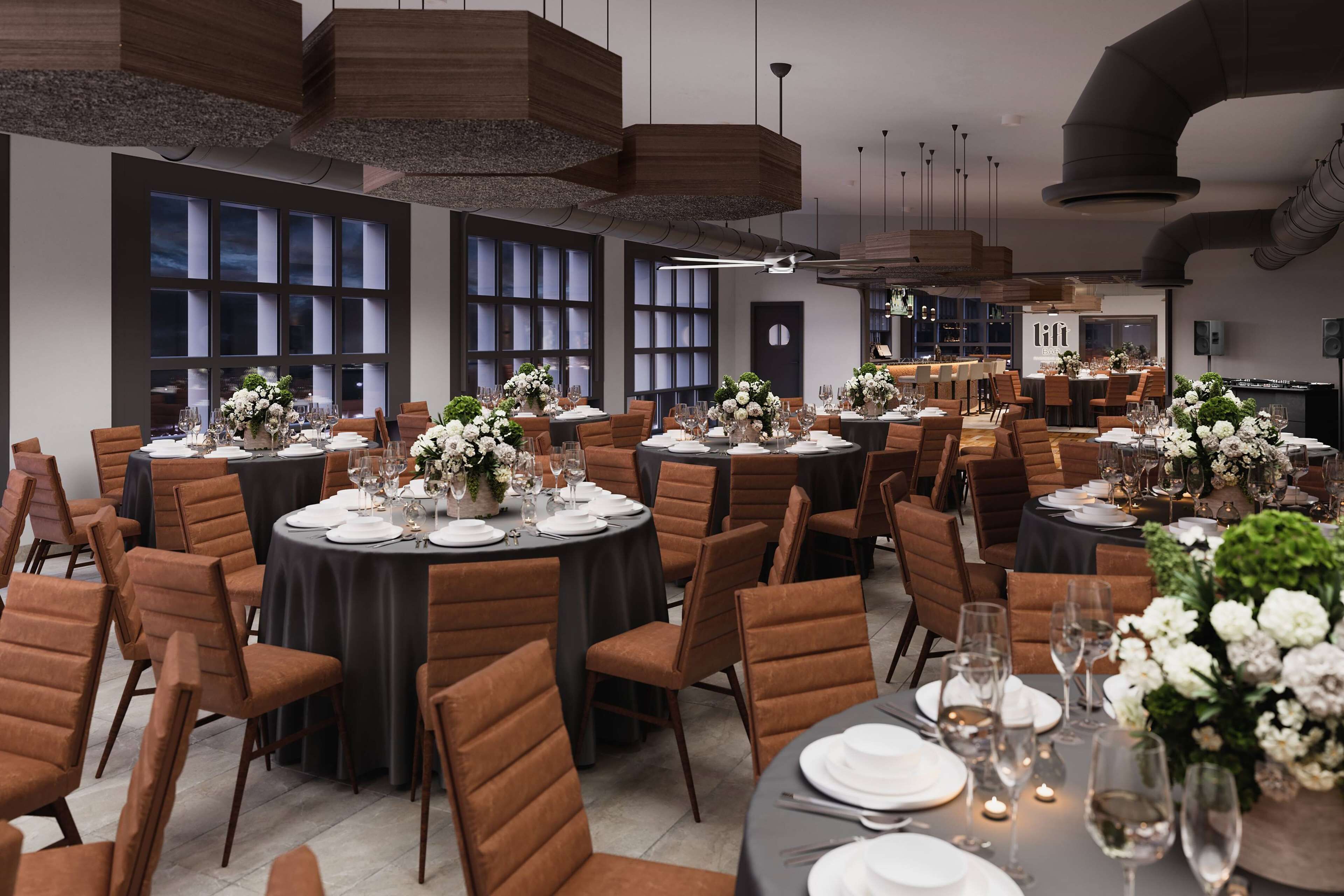 A spacious dining area with round tables set for a formal meal, featuring brown upholstered chairs and elegant floral centerpieces.