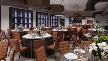 A spacious dining area with round tables set for a formal meal, featuring brown upholstered chairs and elegant floral centerpieces.