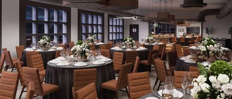 A spacious dining area with round tables set for a formal meal, featuring brown upholstered chairs and elegant floral centerpieces.