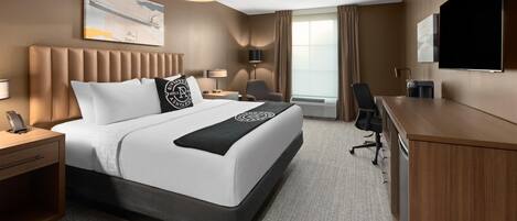 Una habitación de hotel con una cama grande, un escritorio, una silla, un televisor y una ventana con cortinas.
