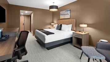 A hotel room with a bed, desk, chair, bedside tables, lamp, and a painting on the wall.