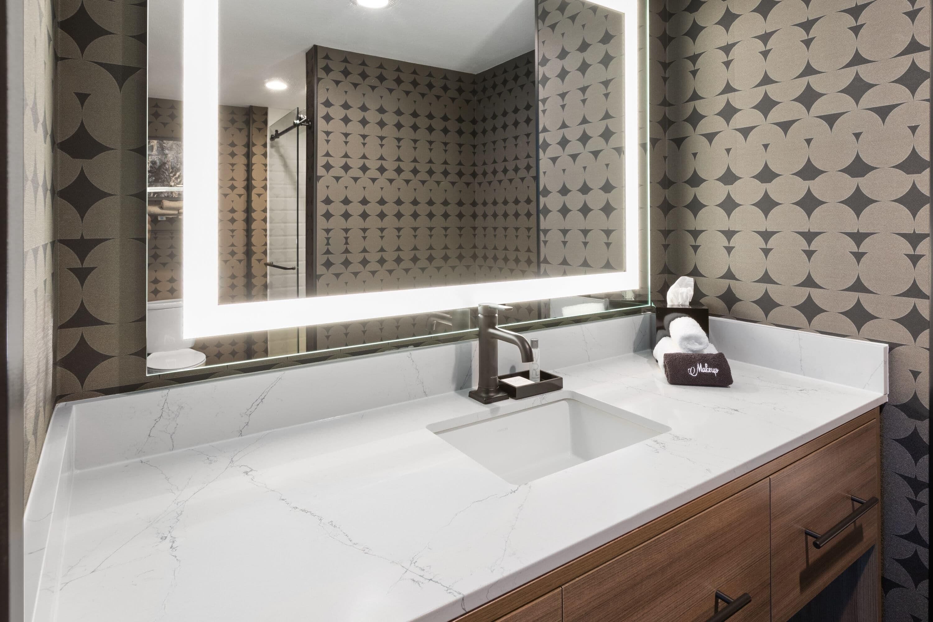 A bathroom with a large mirror, a white marble sink, and a towel holder.
