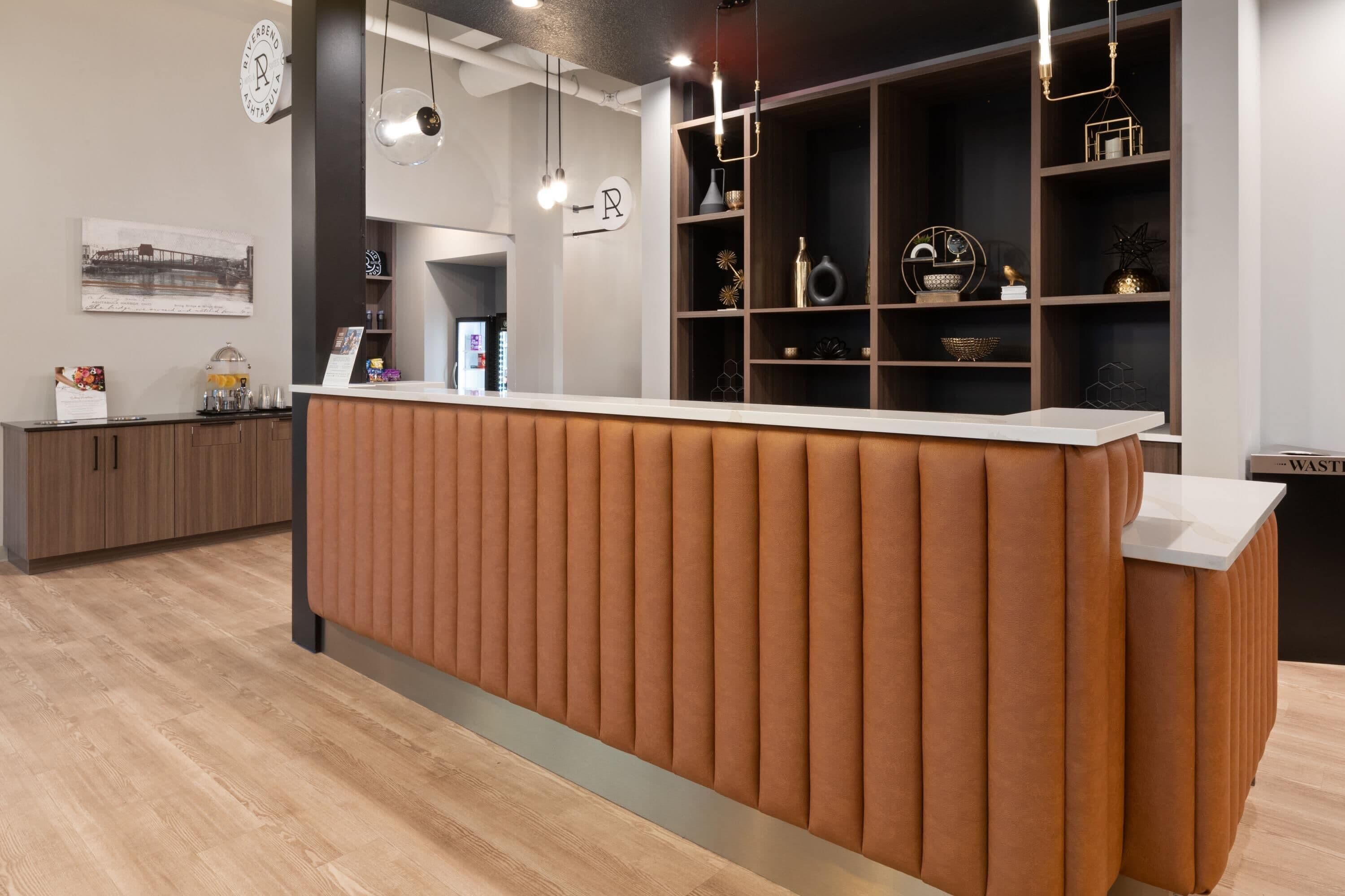 A reception desk with a padded back, a wooden floor, and a wall-mounted sign with a letter.