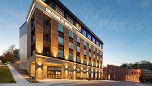 A modern hotel with a brick facade, large windows, and a prominent entrance. - Riverbend Hotel and Suites, Trademark Collection by Wyndham (Ashtabula)