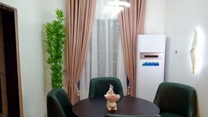 Een eethoek met een ronde tafel, vier stoelen, een decoratief middelpunt, een potplant en een wandairconditioner.