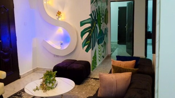 Een moderne woonkamer met een grote, S-vormige lamp, een zwarte bank, een witte salontafel en een grote spiegel.
