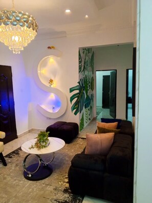 En moderne stue med en stor, S-formet lampe, en sort sofa, et hvidt sofabord og et stort spejl.