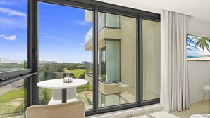 A modern living room with a large sliding glass door leading to a balcony, a round table with a chair, and a flat-screen TV mounted on the wall. - A-405 Stunning one bedroom apartment overlooking the pool (Cupecoy)