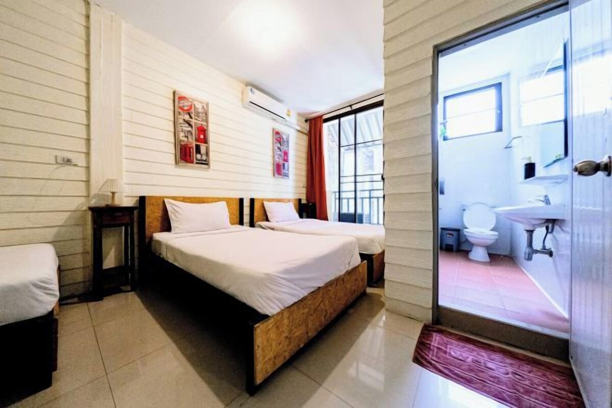 A bedroom with two beds, a window, and a bathroom visible through an open door.