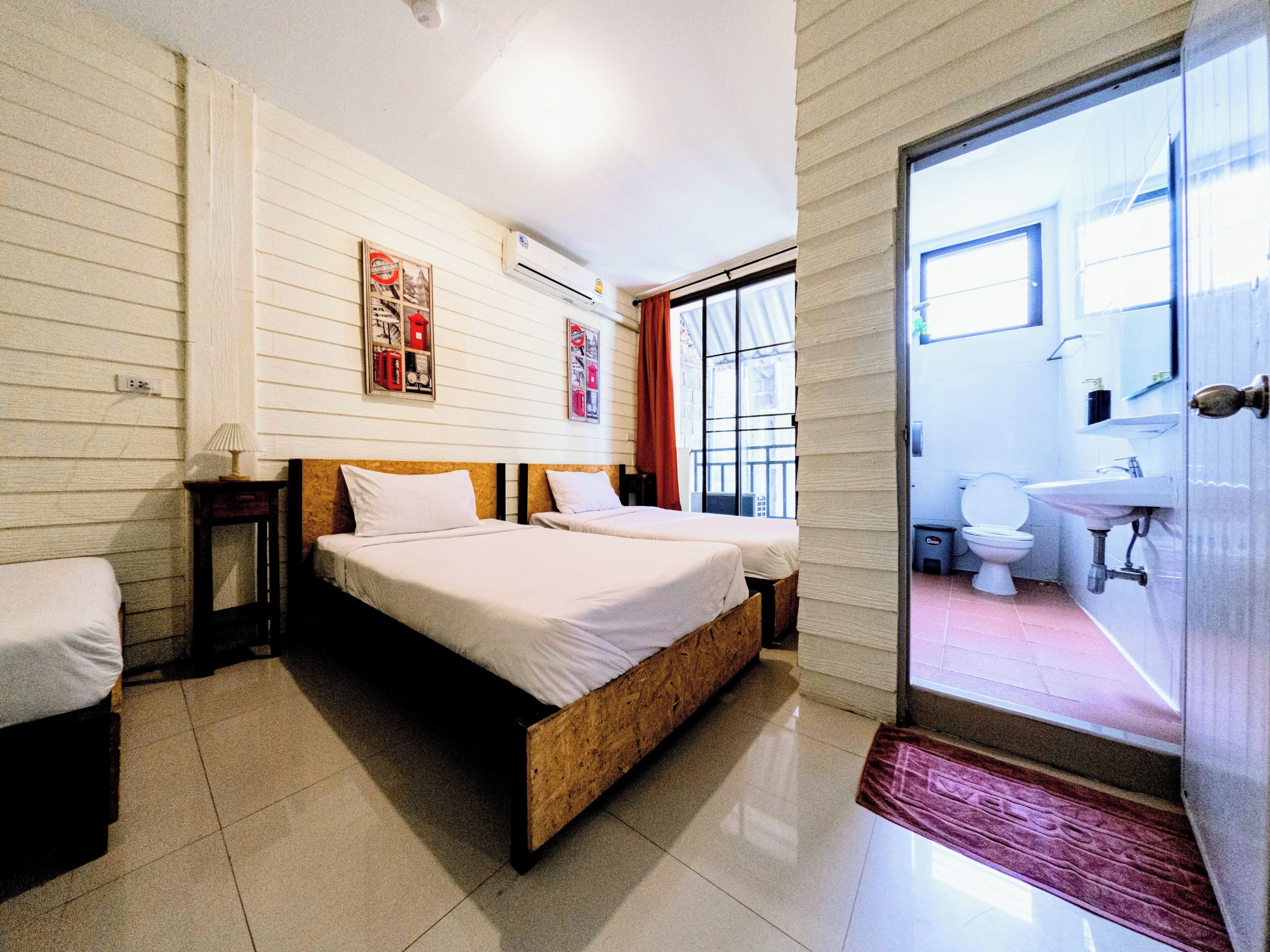 A bedroom with two beds, a bathroom with a sink, and a view through a glass door.