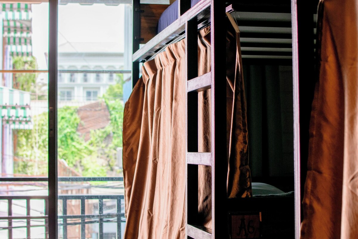 A bunk bed with a view of the outside, a window with curtains, and a door with a sign.