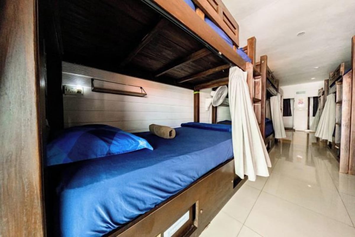 A bunk bed room with a wooden headboard, a blue mattress, and a pillow.