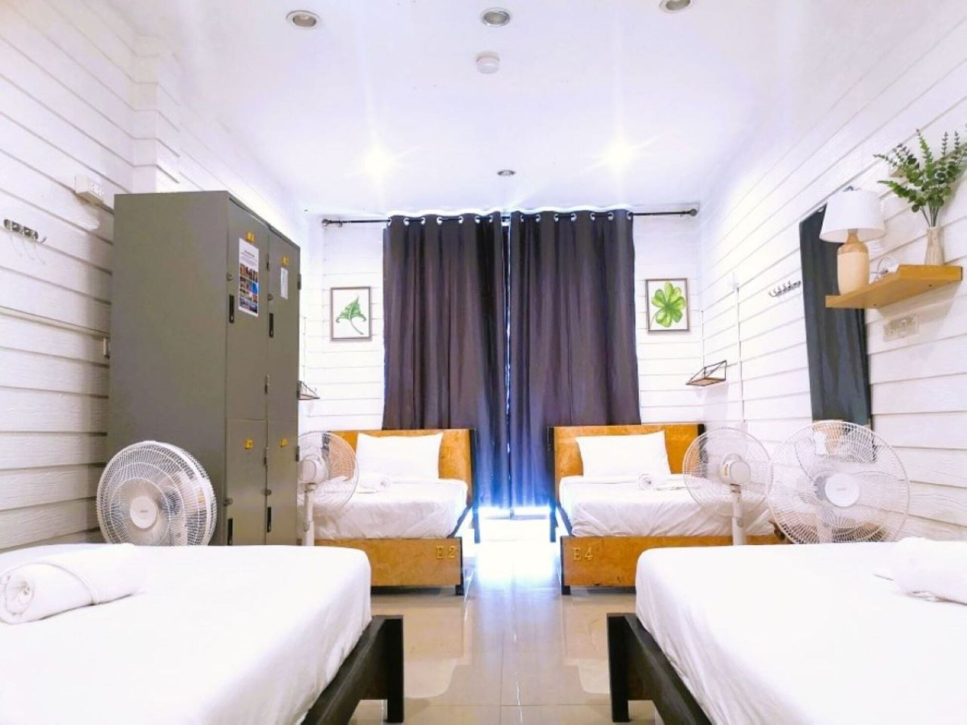 A hotel room with two beds, a wardrobe, a desk, and a window with curtains.