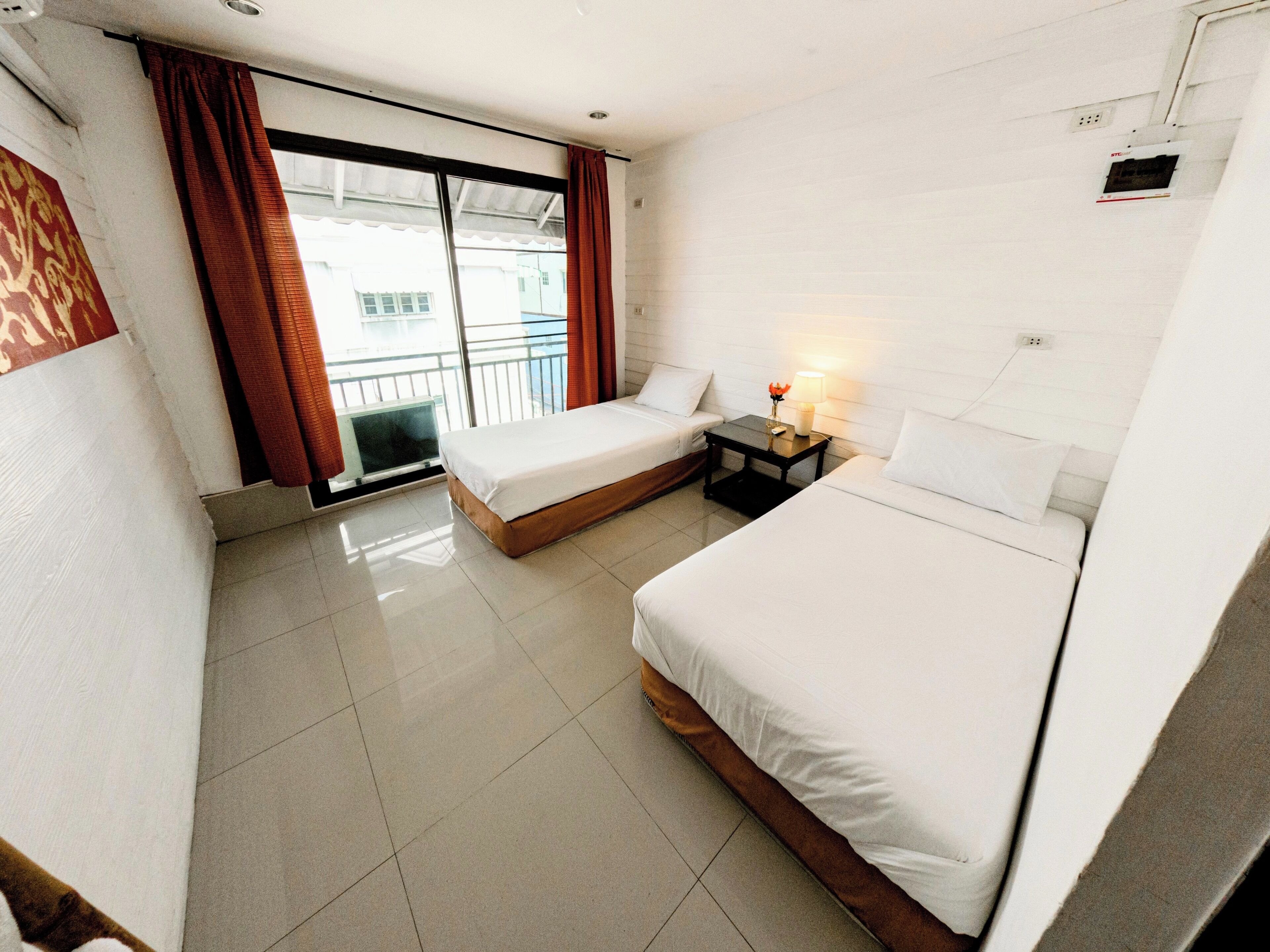 A hotel room with two beds, a small table with a lamp, and a sliding door leading to a balcony.