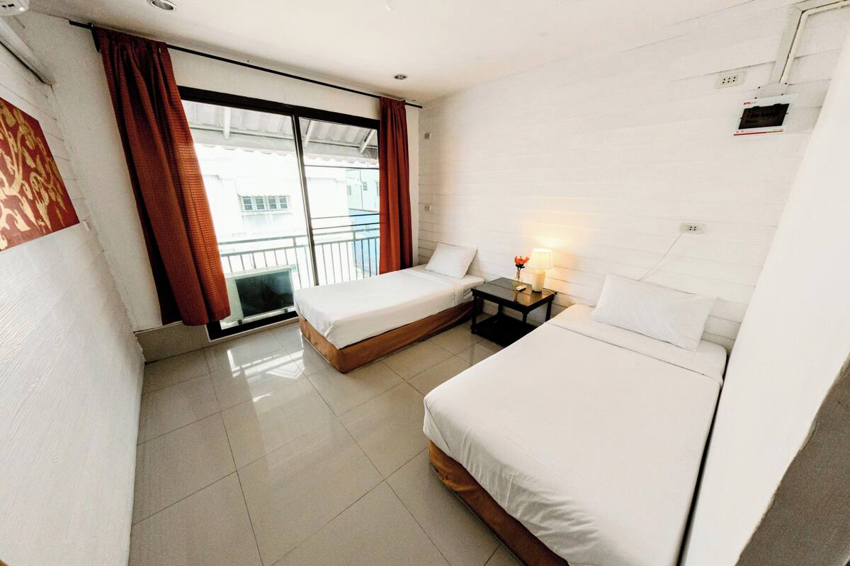 A hotel room with two beds, a small table with a lamp, and a sliding door leading to a balcony.