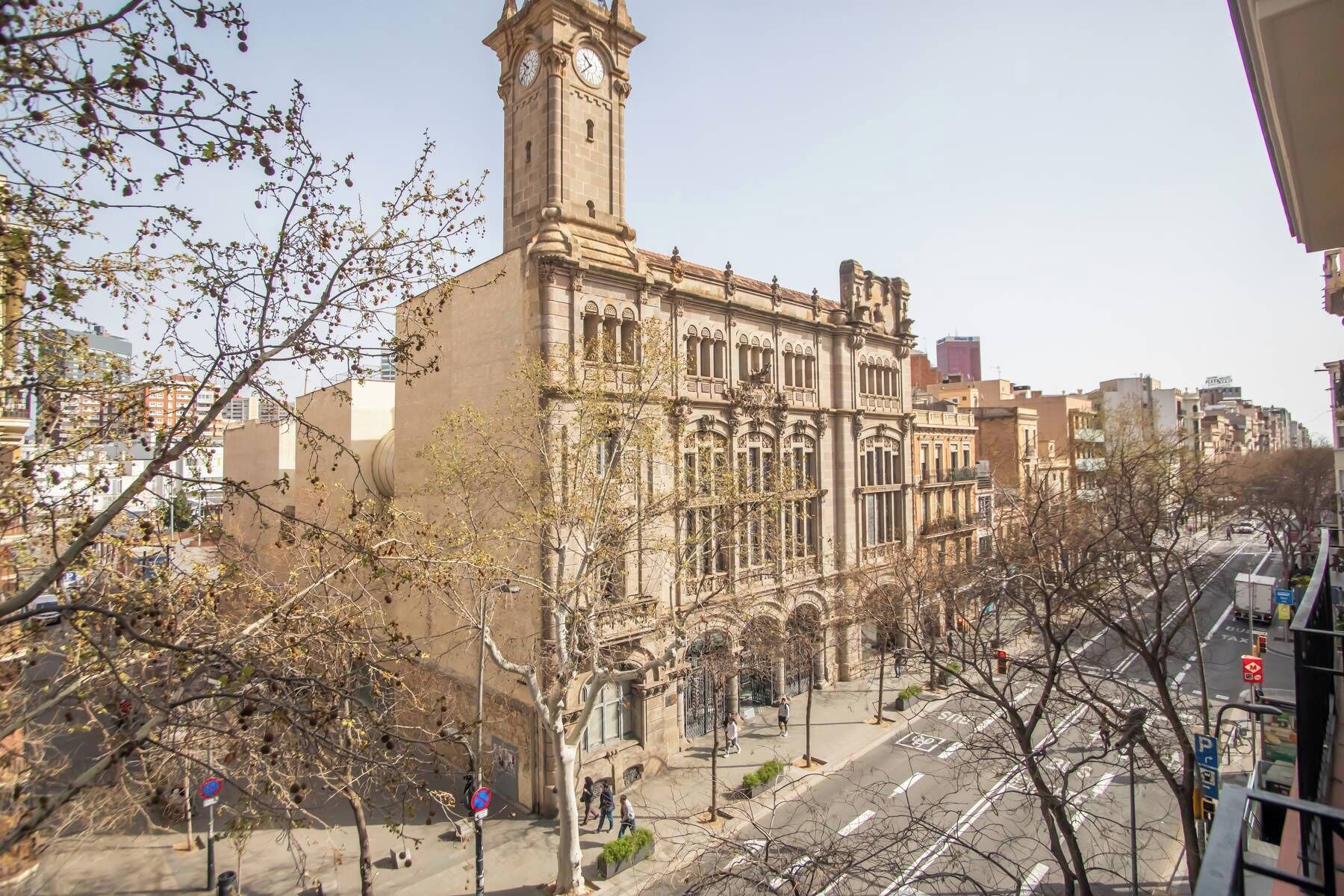 Un edificio histórico con una torre de reloj, arquitectura ornamentada y una vista de la calle con peatones y vehículos.