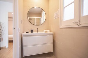 Un baño con un tocador blanco, un espejo redondo y una ventana.