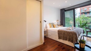 A modern bedroom with a large bed, a bedside table, a lamp, and a view of a balcony.