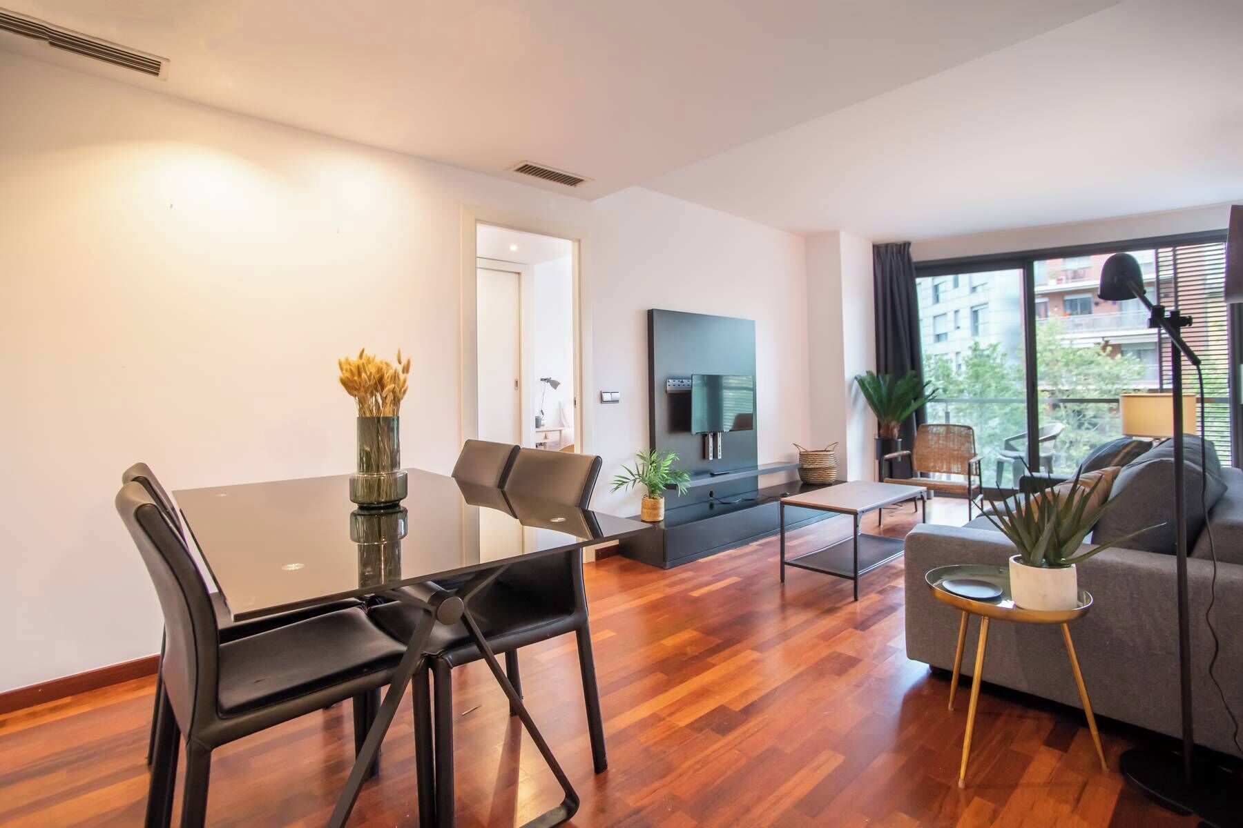 Een moderne woonkamer met een eetgedeelte, een flatscreen televisie aan de muur en een groot raam met uitzicht op de stad.