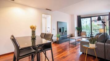 Een moderne woonkamer met een eetgedeelte, een flatscreen televisie aan de muur en een groot raam met uitzicht op de stad.