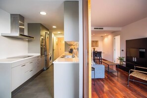 A modern kitchen with a central island, stainless steel appliances, and a dining area with a dark sofa and a small table. - 42BADR1040 - New & Bright Apartment PobleNou (Barcelona)