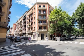 Un edificio de varios pisos con balcones, un paso de peatones y coches aparcados.