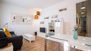 A modern living room with a sofa, a coffee table, a TV, a bookshelf, and a dining area with a table and chairs. - P2VIIV1042  - Modern & Cozy Apartment Poble Sec (Barcelona)