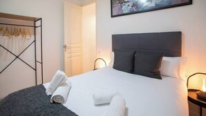 A neatly made bed with white linens and two pillows, a framed picture on the wall, and a coat rack with hangers. - P2VIIV1042  - Modern & Cozy Apartment Poble Sec (Barcelona)