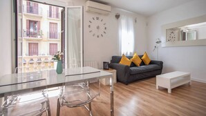 A modern living room with a glass dining table, a gray sofa with yellow cushions, and a white side table. - P2VIIV1042  - Modern & Cozy Apartment Poble Sec (Barcelona)