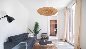 Ett modernt vardagsrum med en grå soffa, ett litet sidobord, en vävd taklampa och utsikt över en garderob och en skjutdörr i glas.