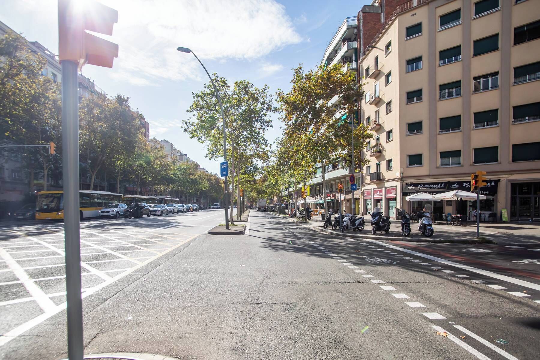 Une vue de rue avec un passage piéton, des voitures garées et des immeubles abritant des boutiques et des cafés.