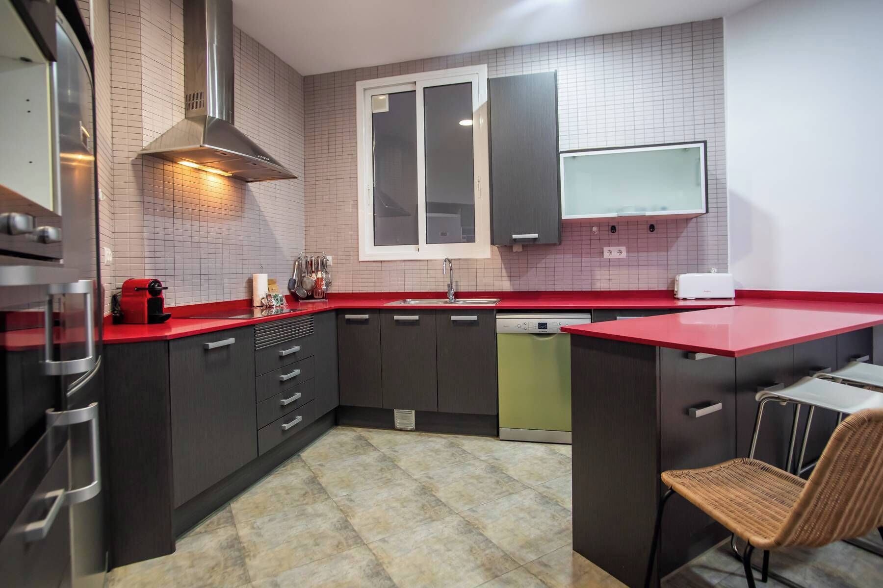 A modern kitchen with dark cabinets, a red countertop, a built-in stove, and a window above the sink.