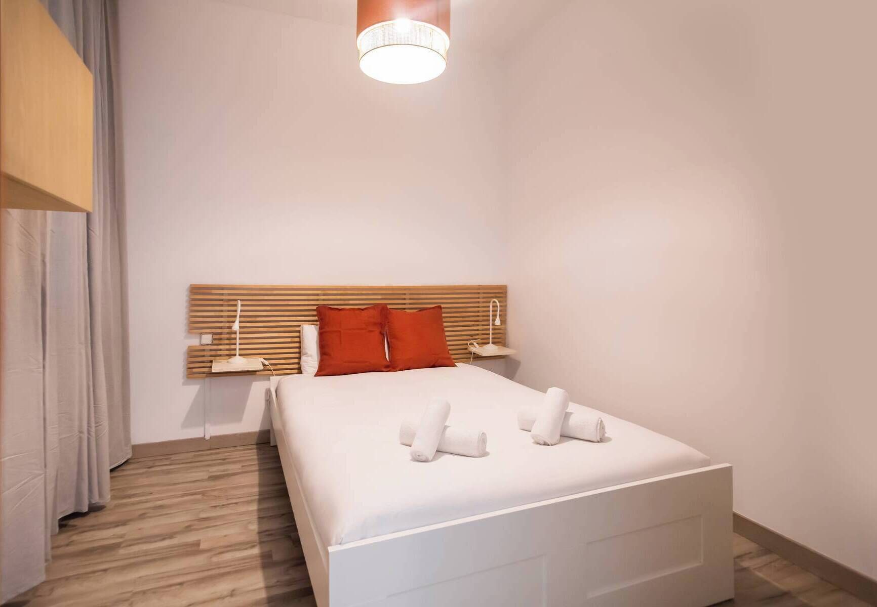 Une chambre d’hôtel moderne avec un grand lit, une tête de lit en bois, du linge de lit blanc et deux tables de chevet avec des lampes.