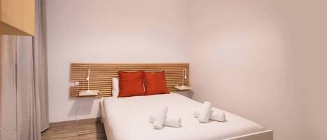 Une chambre d’hôtel moderne avec un grand lit, une tête de lit en bois, du linge de lit blanc et deux tables de chevet avec des lampes.