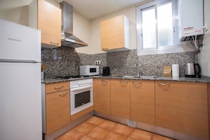 A compact kitchen with a built-in oven, microwave, and stove, wooden cabinets, and a window with blinds.