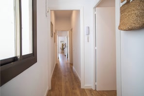 A narrow hallway with wooden flooring, white walls, and a door at the end.