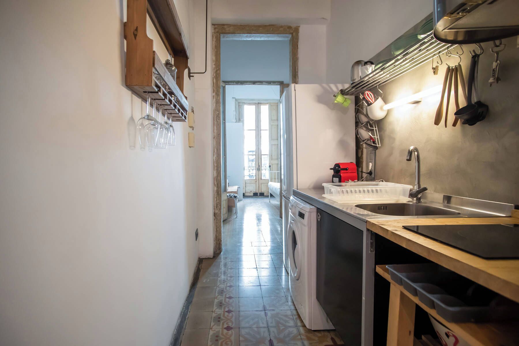 A narrow kitchen with a washing machine, a sink, and a drying rack.