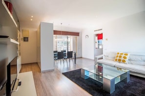 A modern living room with a glass coffee table, a white sofa with yellow cushions, and a dining area with a glass table and chairs.