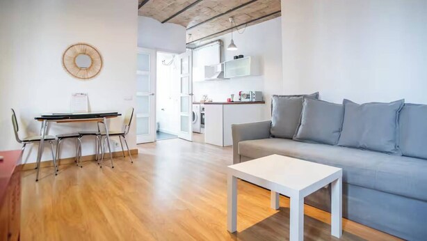 A modern living room with a sofa, a dining table with chairs, and a kitchen in the background.