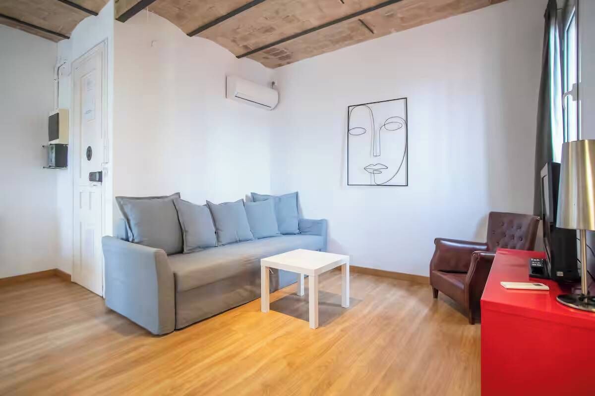 Un salon avec un canapé gris, une table basse blanche, une table d’appoint rouge avec une lampe, et un fauteuil marron.