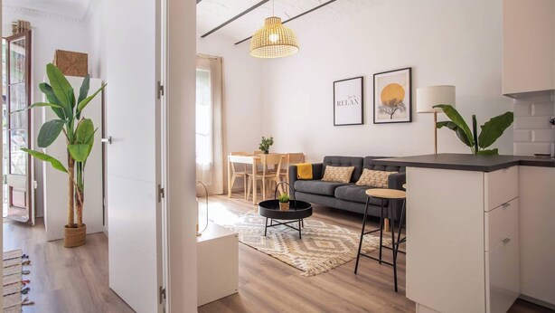 A modern living room with a sofa, coffee table, and pendant light. There is a dining area with a table and chairs, and a kitchen area with cabinets and a countertop. - 12par1003- Luminoso piso en Paralelo (Barcelona)