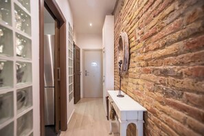 Een smalle gang met een bakstenen muur, een witte console tafel en een deur aan het einde.