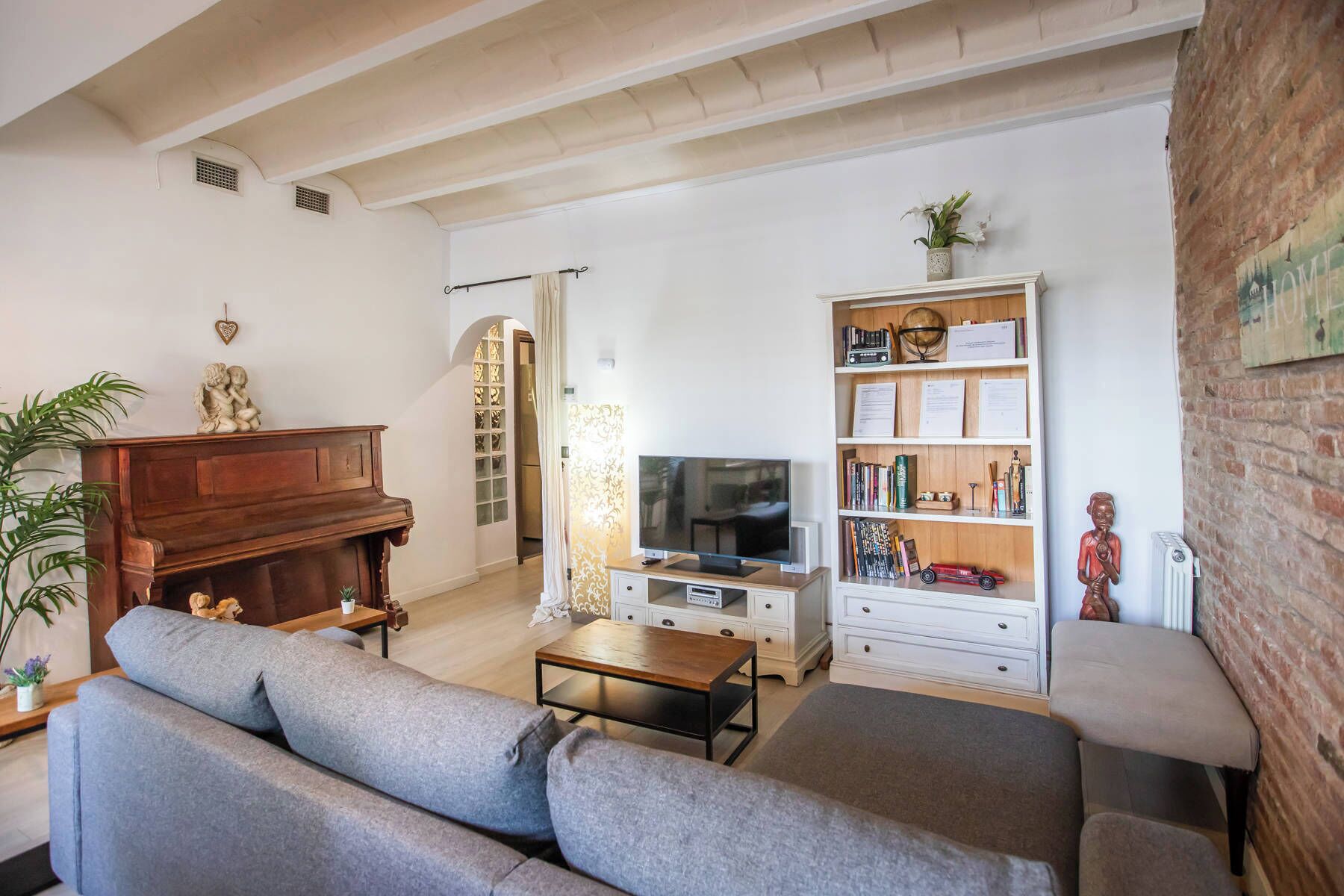 A living room with a piano, sofa, TV, bookshelf, and a brick wall.