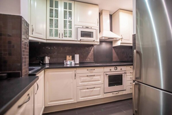 Een keuken met witte kasten, een roestvrijstalen koelkast, een magnetron en een fornuis.